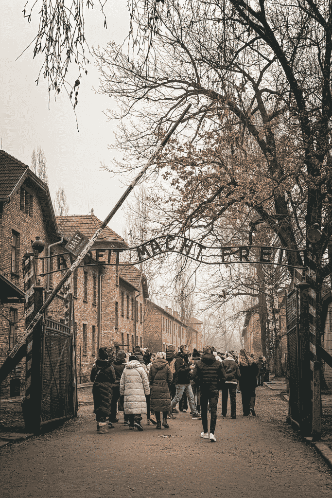The entrance to Auschwitz I concentration camp in Poland, with visitors walking beneath the “Arbeit Macht Frei” gate.