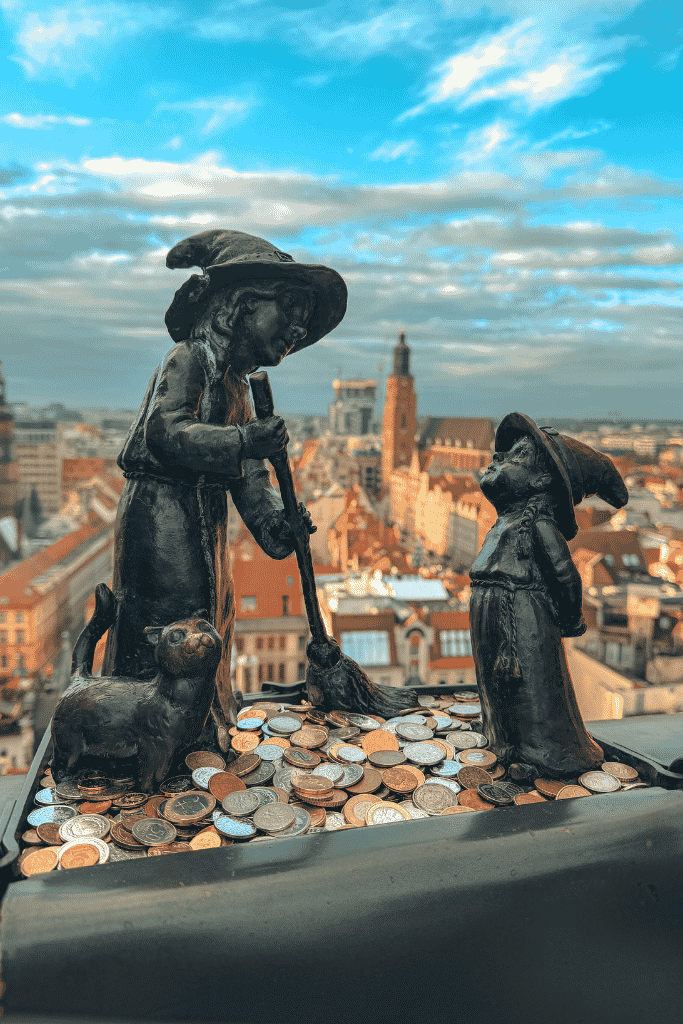 Wroclaw dwarf statues surrounded by coins with panoramic views of the city’s Old Town in the background.
