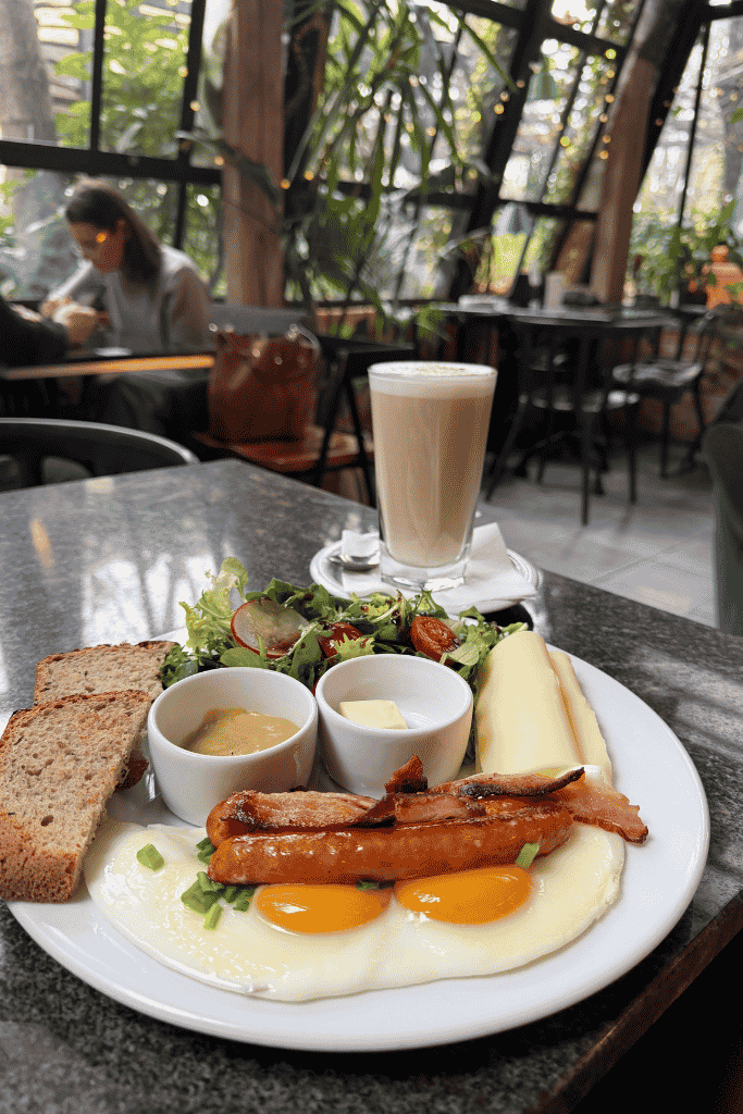 Breakfast with fried eggs, sausages, bacon, bread, salad, cheese, and a latte in Wroclaw, Poland.