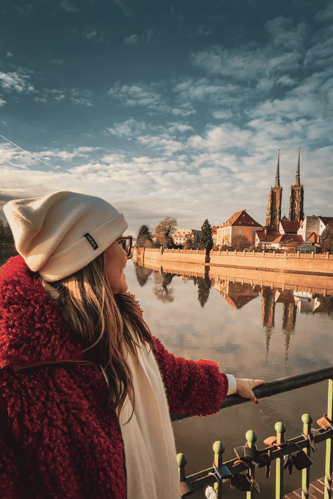 Kate overlooking the Oder River in Wroclaw, Poland, with the twin spires of the Cathedral of St. John the Baptist reflected in the water.