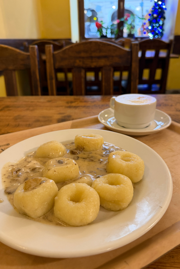 A plate of traditional Polish dumplings with creamy mushroom sauce and coffee at a milk bar in Krakow, Poland.
