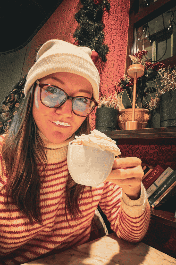 Kate enjoying a cup of hot chocolate topped with whipped cream inside a cozy, festively decorated café in Wroclaw, Poland.