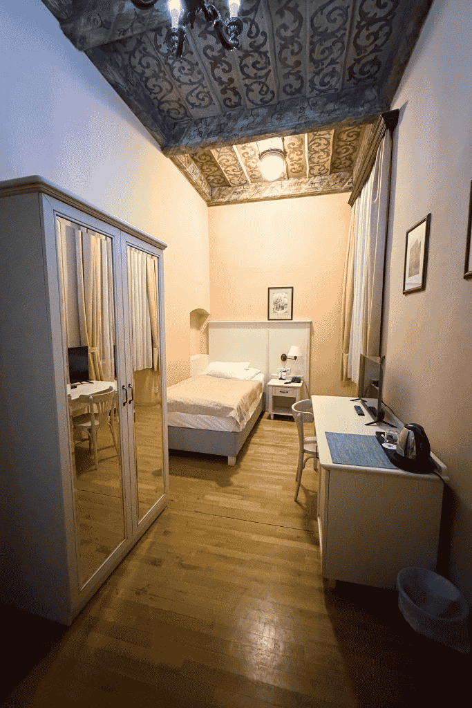 Guest room at Hotel Černý Slon in Prague, featuring a single bed, mirrored wardrobe, desk, and ornate historic ceiling.