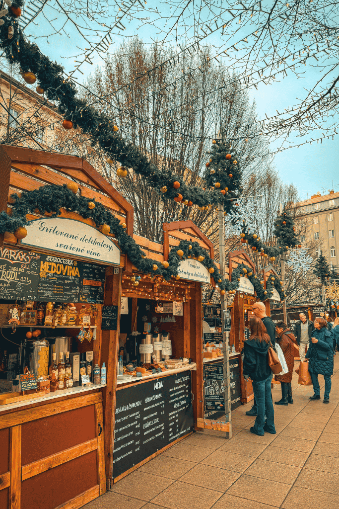 Christmas market stalls decorated with evergreen garlands and ornaments, selling hot mead, mulled wine, and other festive treats in Prague.