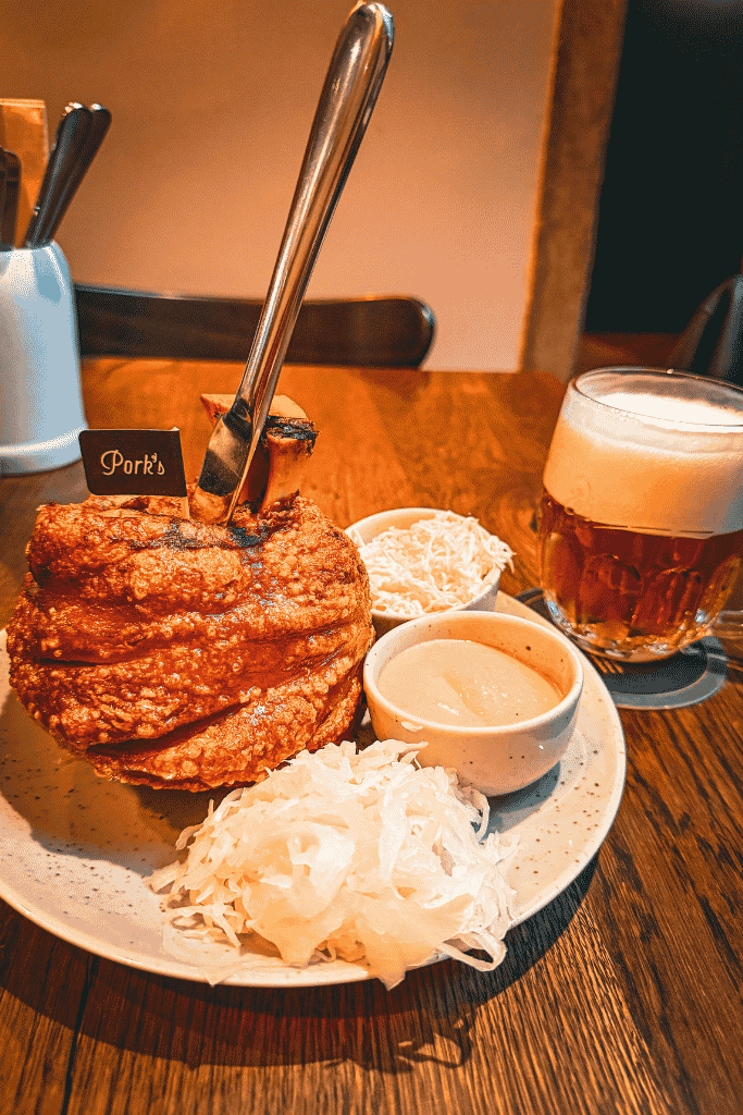 A hearty Czech pork knuckle served with sauerkraut, creamy mustard, horseradish, and a cold Czech beer.