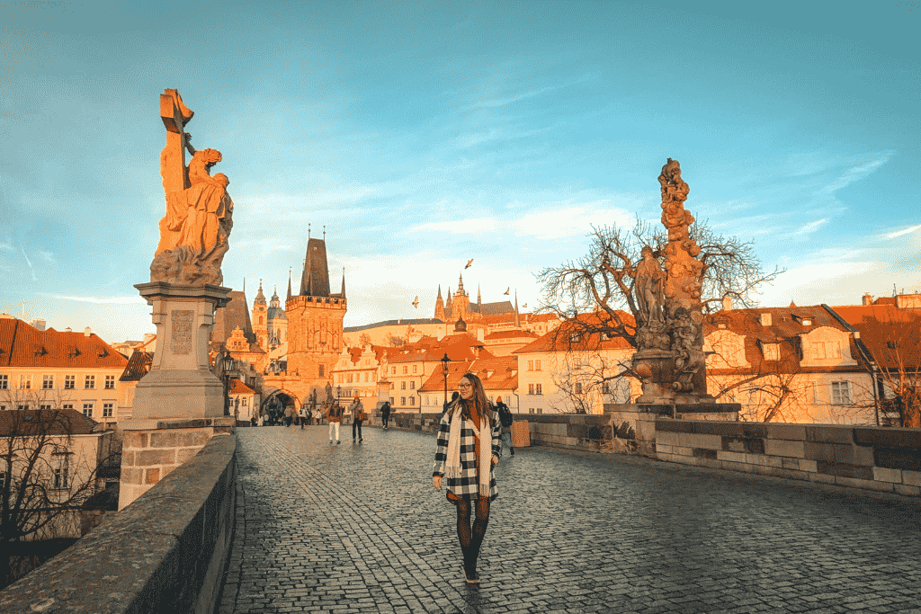 Walking across Prague’s iconic Charles Bridge in the golden morning light, with Prague Castle rising above the city in the distance.