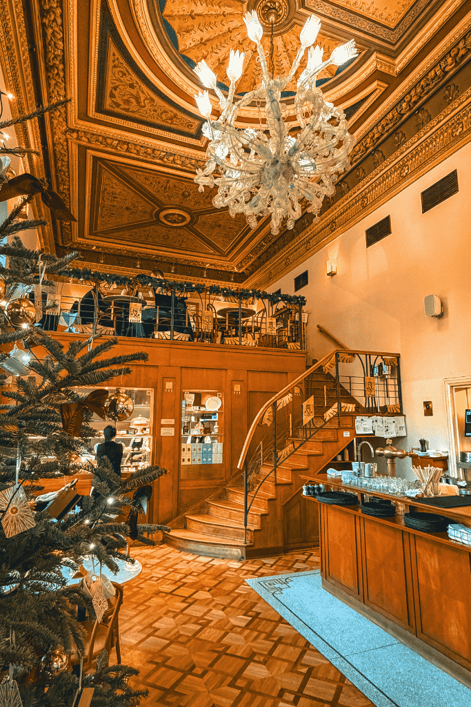A festive stop inside one of Prague’s elegant historic cafés, complete with an ornate ceiling, sparkling chandelier, and Christmas tree.
