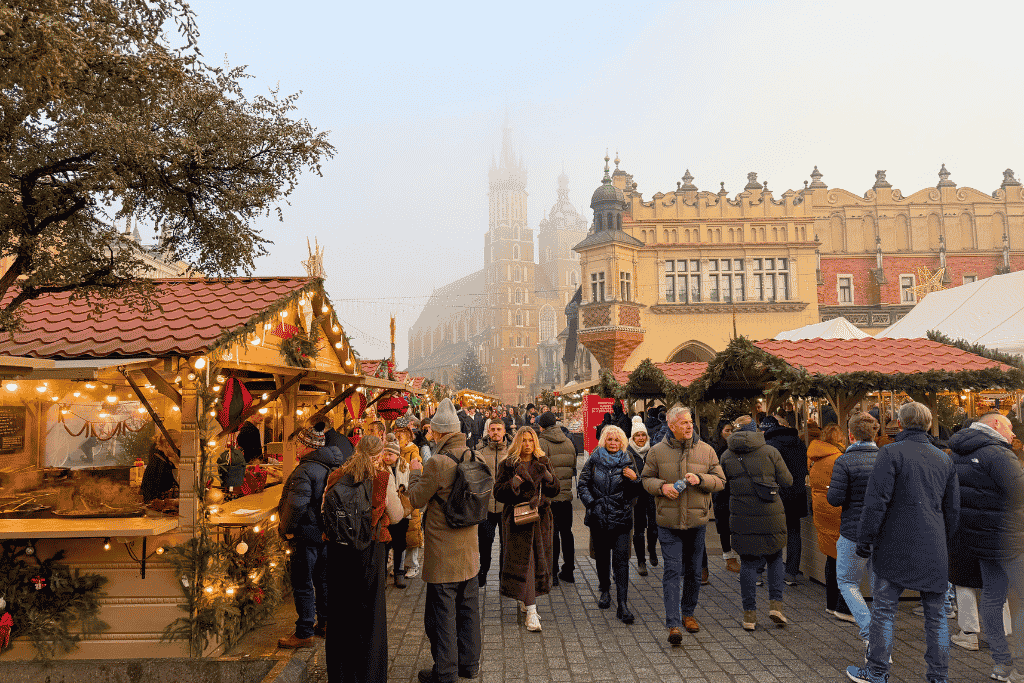 Krakow Christmas Market in Main Market Square with festive wooden stalls, the Cloth Hall, and St. Mary’s Basilica rising through the fog.