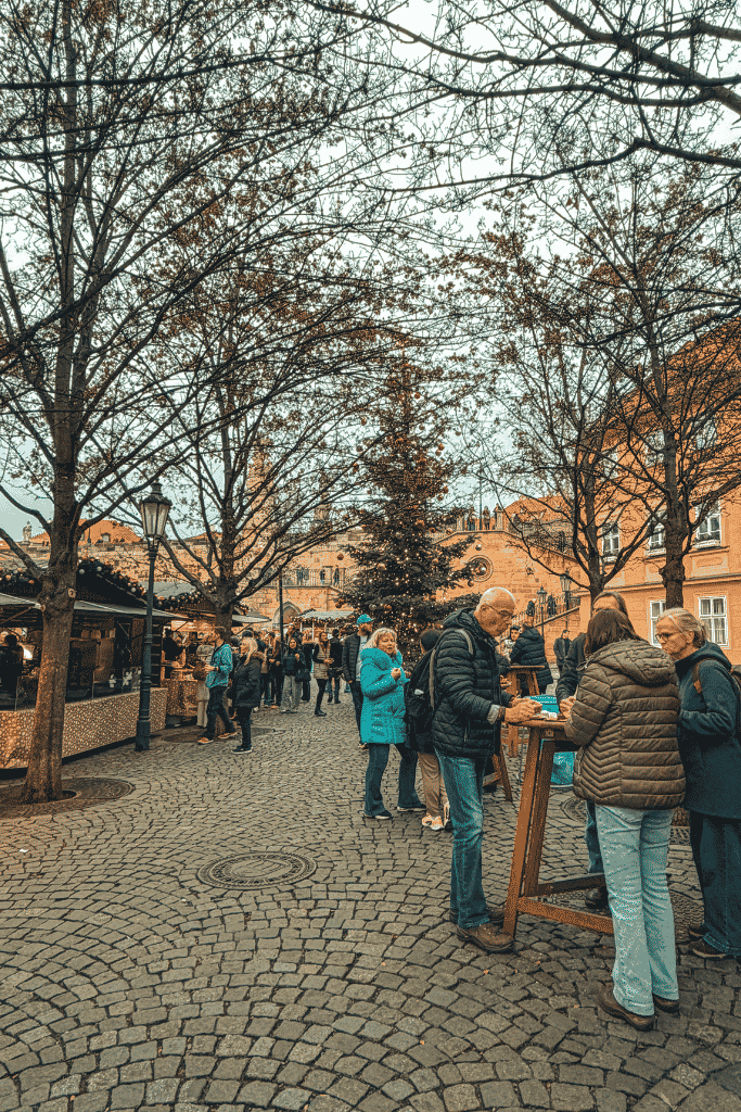 A cozy Christmas market in Lesser Town, where festive wooden stalls and a glowing Christmas tree create a charming holiday atmosphere.