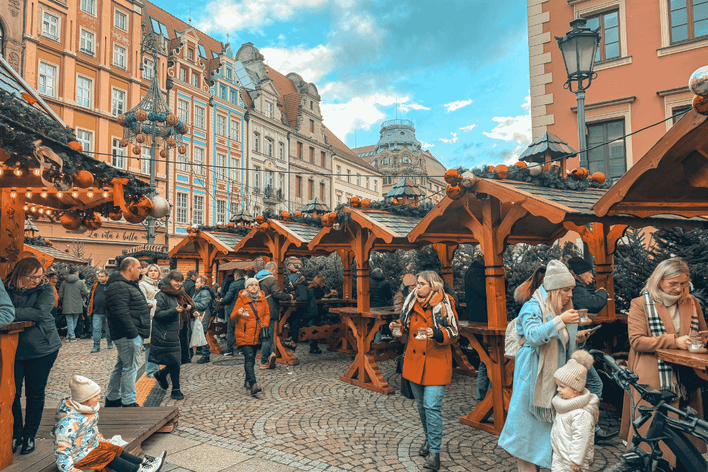 A busy European Christmas market filled with wooden stalls, festive decorations, and visitors exploring a colorful historic Old Town square.