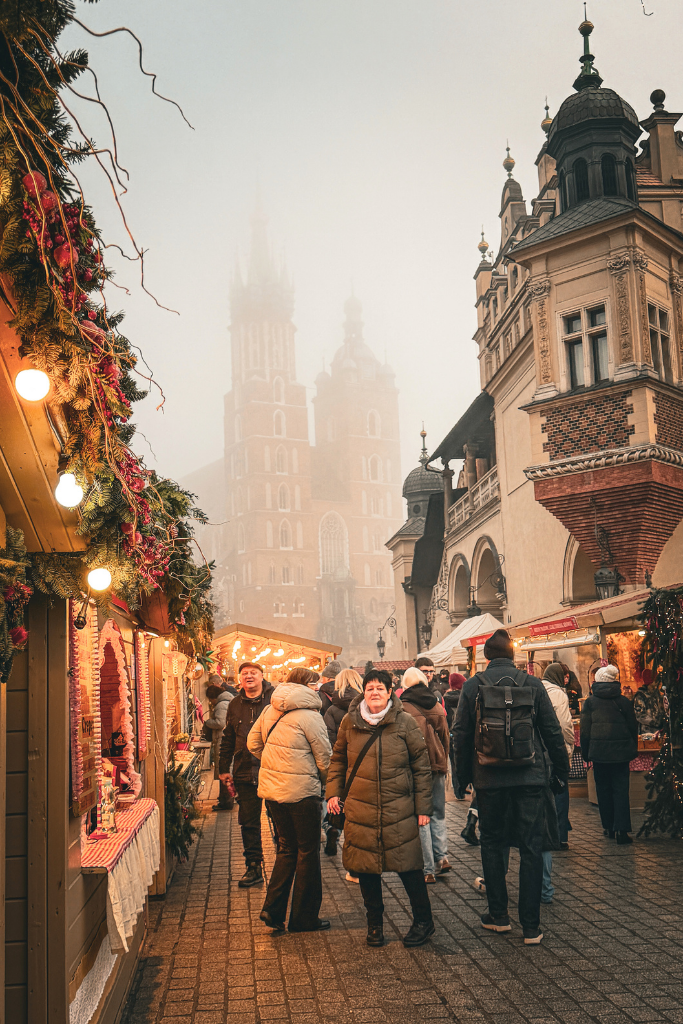 A festive Christmas market in Krakow’s Main Market Square with St. Mary’s Basilica rising through the fog behind the wooden stalls.