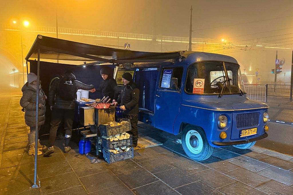 Blue vintage food truck grilling Polish sausages on a foggy evening in Krakow.