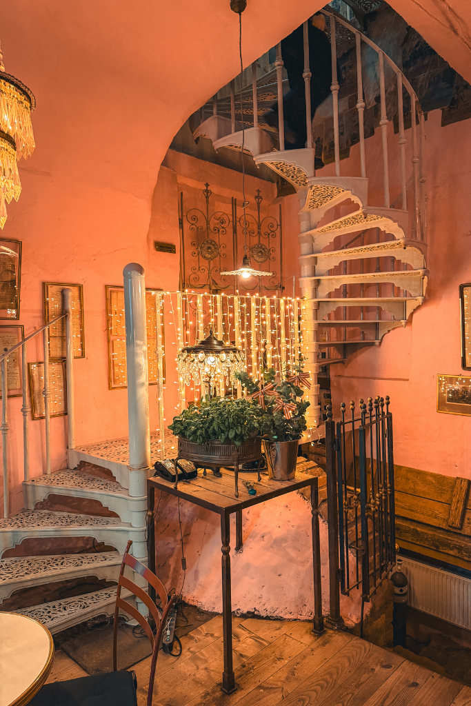 Cozy interior of Camelot Cafe in Krakow with a spiral staircase, antique details, and Christmas lights.