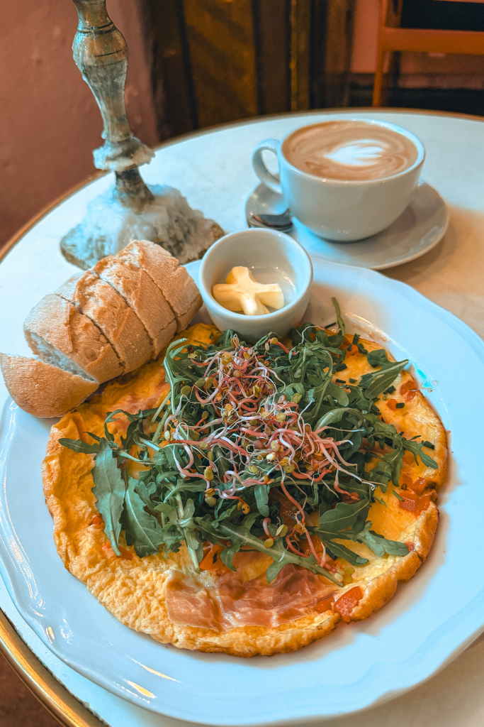 Omelet topped with fresh greens and sprouts, served with bread and a cappuccino at Camelot Cafe in Krakow.