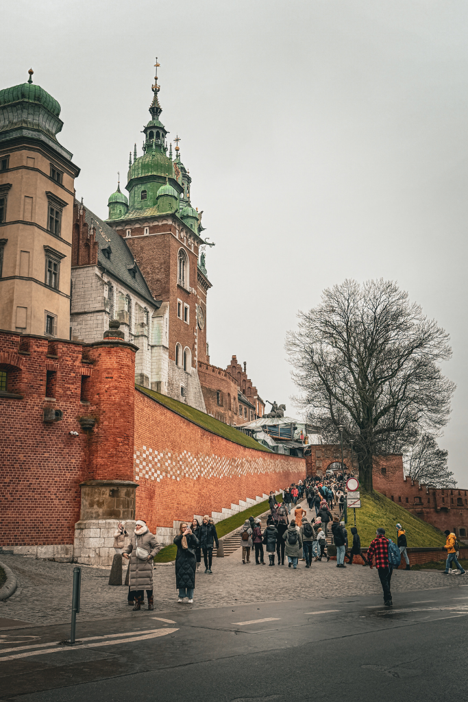 Visitors walking up the path toward Wawel Royal Castle in Krakow on a cloudy winter day.