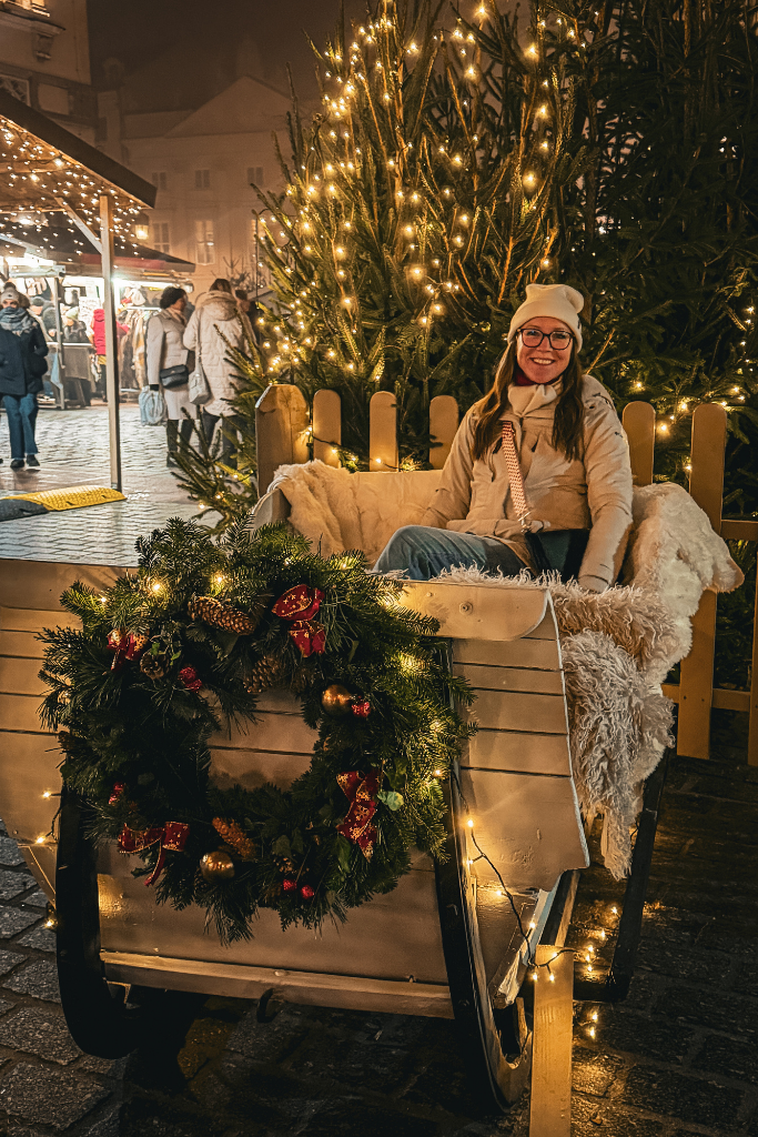 Kate sitting in a festive sleigh surrounded by Christmas trees and twinkling lights at the Krakow Christmas market.