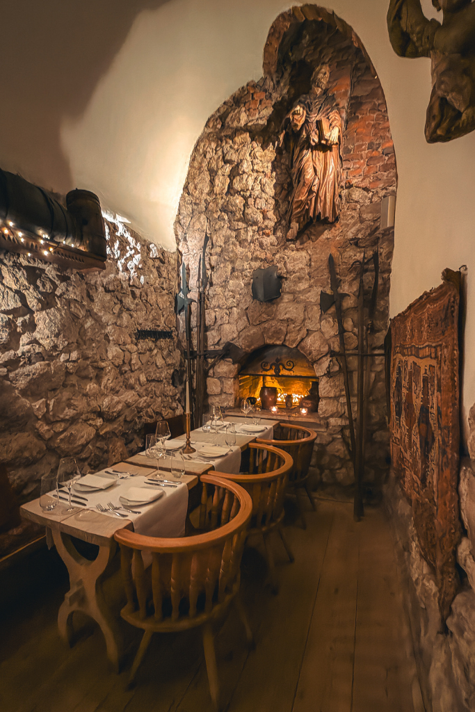 Cozy stone-walled dining room with a glowing fireplace inside Pod Aniołami restaurant in Krakow.