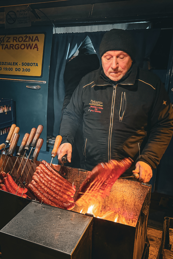 Vendor grilling Polish sausages over an open fire at a street food stand in Krakow.