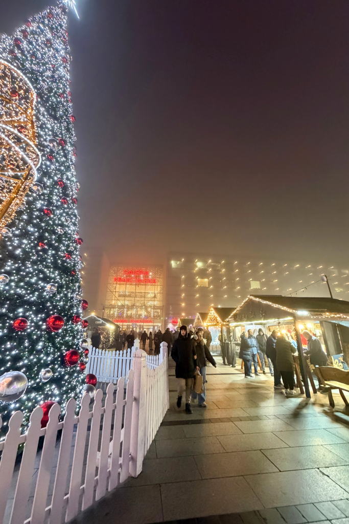 Krakow train station Christmas Market at night with festive stalls, glowing lights, and a towering Christmas tree.
