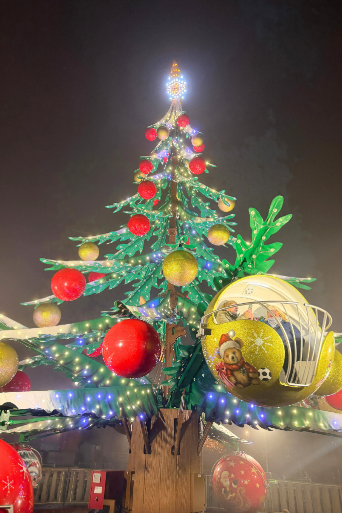 Christmas tree-themed carnival ride glowing with colorful ornaments at Krakow’s train station Christmas Market.