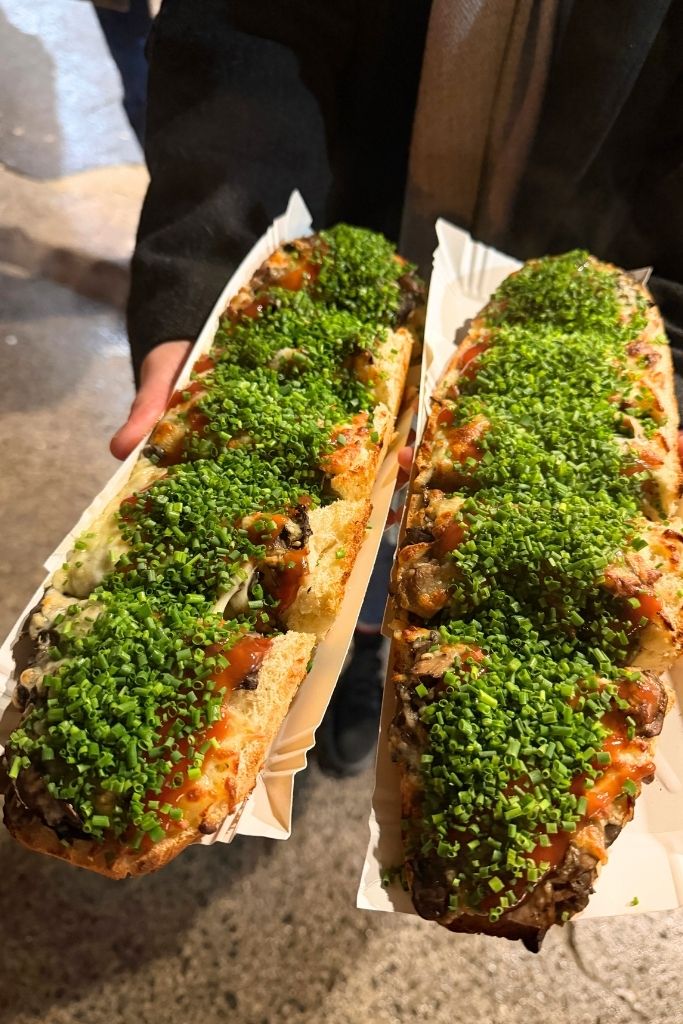 Traditional Polish zapiekanka topped with mushrooms, melted cheese, sauce, and fresh chives in Krakow.