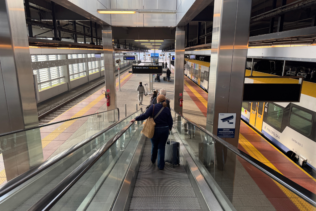 Travelers with luggage heading down to the train platform at Krakow Airport railway station.