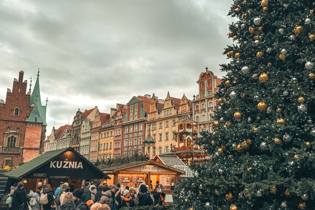 Wroclaw Christmas Market with a towering decorated Christmas tree, festive stalls, and colorful Old Town buildings.