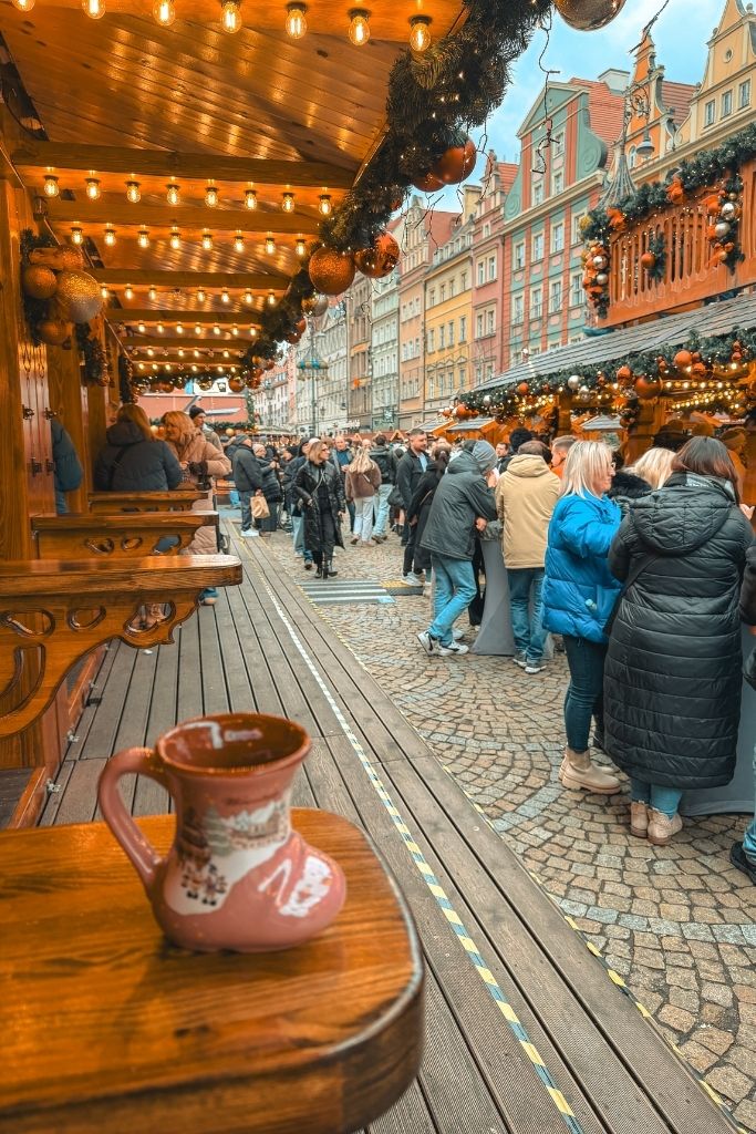 Wroclaw Christmas Market with a collectible boot-shaped mug, festive wooden stalls, and colorful Old Town buildings.