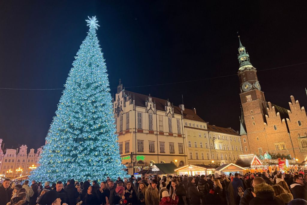 Giant illuminated Christmas tree at Wroclaw Christmas Market at night with the historic Old Town Hall and festive market stalls.