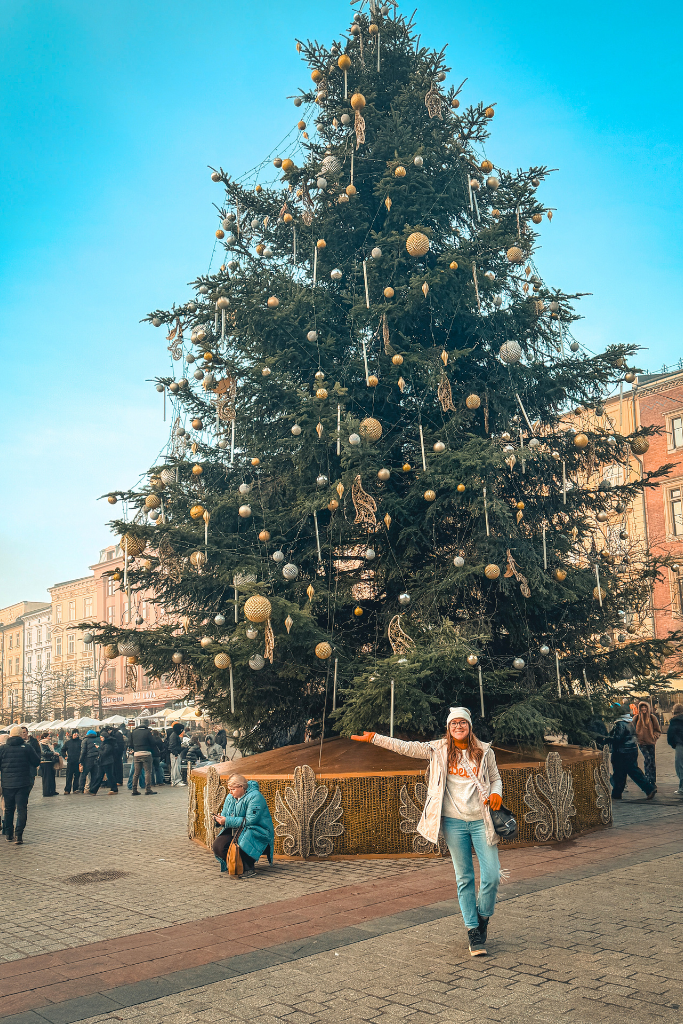 Kate standing beside a towering Christmas tree at Krakow Christmas Market in the Main Market Square.