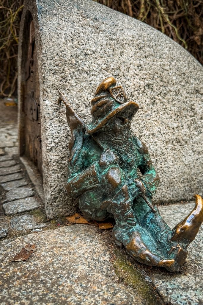 Bronze Wroclaw dwarf statue dressed as a wizard sitting against his stone house in Wroclaw, Poland.