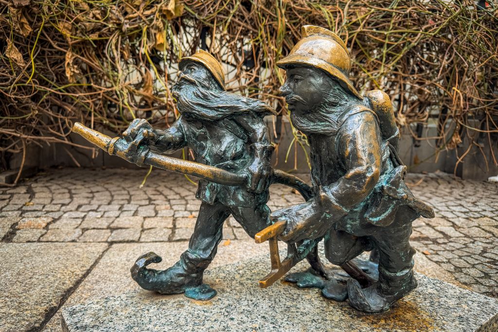Two bronze Wroclaw dwarf statues dressed as firefighters carrying equipment through the city.