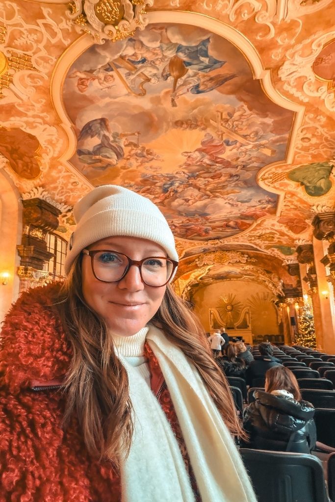 Kate inside an ornate hall at the University of Wroclaw, surrounded by colorful Baroque frescoes and decorative details.