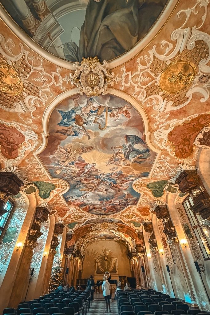 Ornate Baroque interior of Aula Leopoldina at the University of Wroclaw, featuring elaborate ceiling frescoes, sculptures, and gilded details.