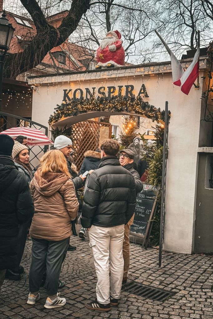 Visitors waiting outside Konspira restaurant in Wroclaw, decorated with Christmas lights, garland, and a Santa figure.