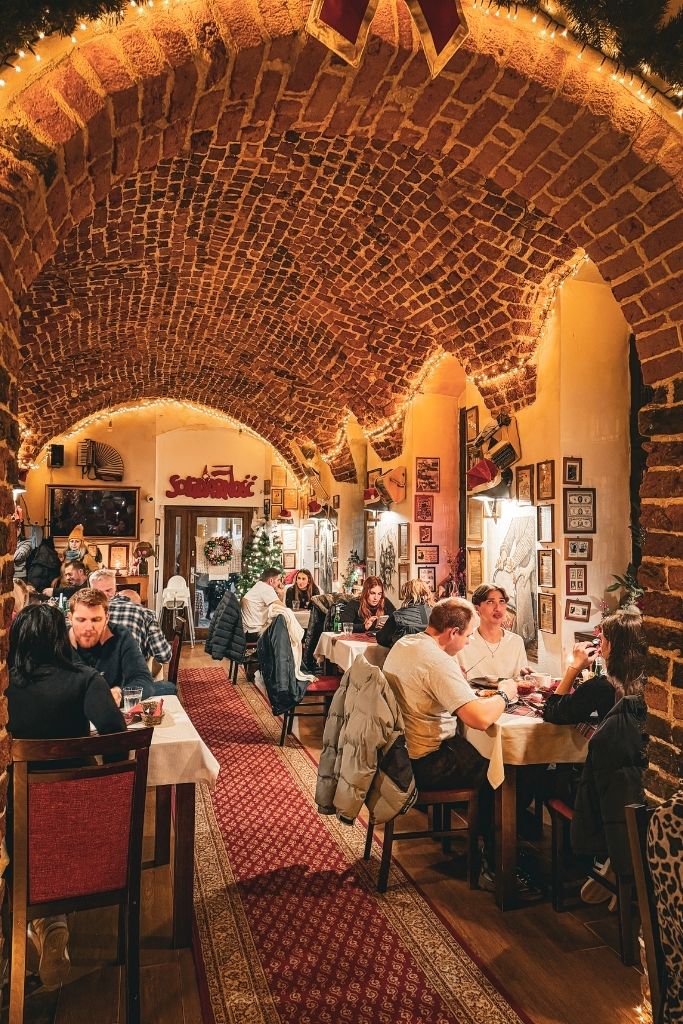 Cozy interior of Konspira restaurant in Wroclaw with brick vaulted ceilings, Christmas lights, and diners at tables.