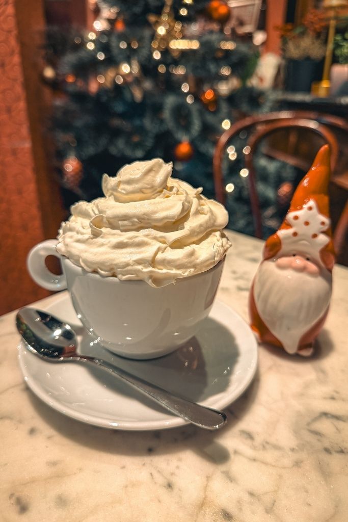 Rich hot chocolate topped with whipped cream beside a Christmas gnome at Czekoladziarnia in Wroclaw.