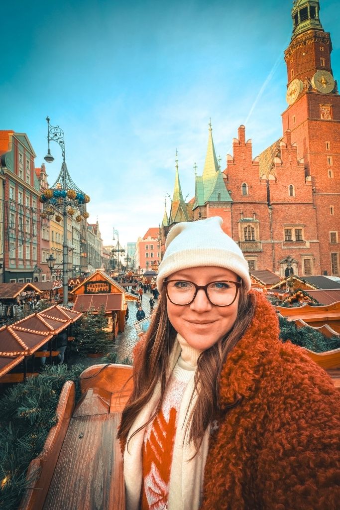 Kate overlooking Wroclaw Christmas Market with the historic Old Town Hall and festive wooden stalls behind her.