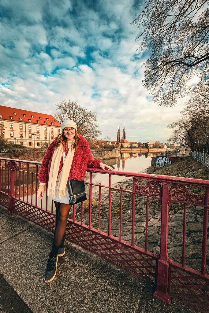 Kate wearing a red teddy coat, white knit beanie, cream scarf, black tights, and black winter boots while exploring Wroclaw in winter.