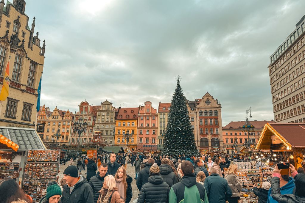 Wroclaw Christmas Market with a large Christmas tree, colorful Old Town buildings, festive stalls, and crowds in Market Square.